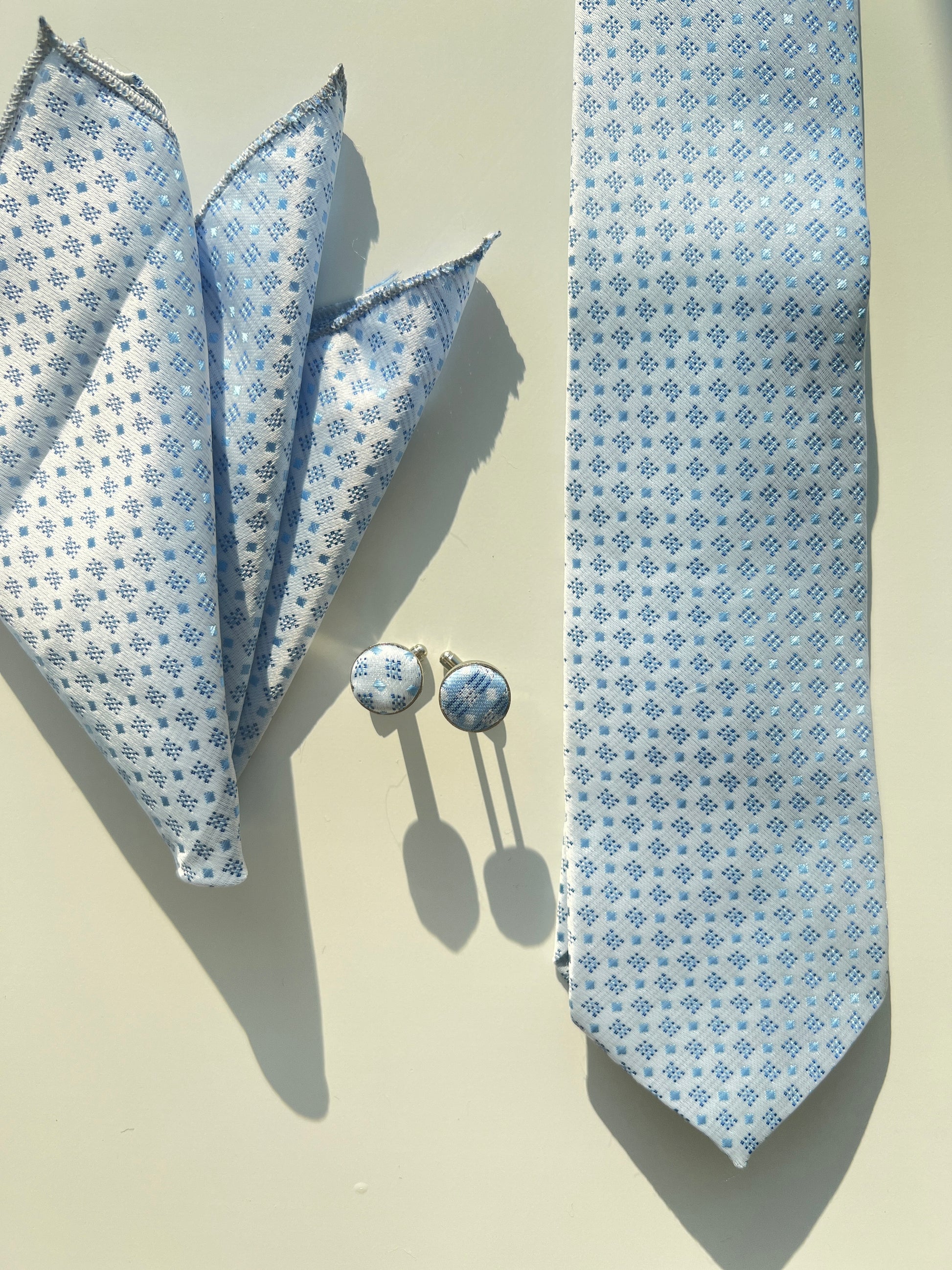 Sophisticated blue snowflake pattern silk tie set with matching cufflinks and pocket square on a light background.