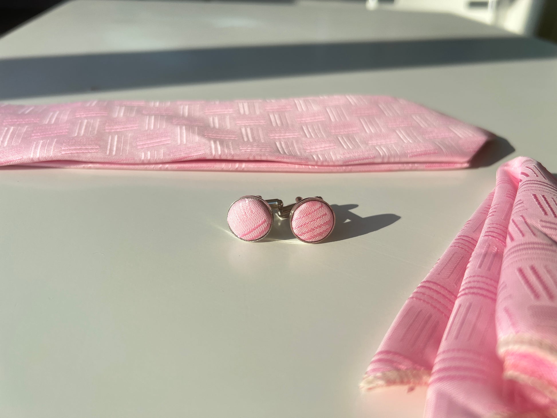 Close-up of the pink silk tie's textured pattern on matching cufflinks