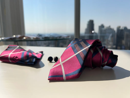 Elegant presentation of the pink and navy striped tie rolled next to matching cufflinks and pocket square, set against a cityscape