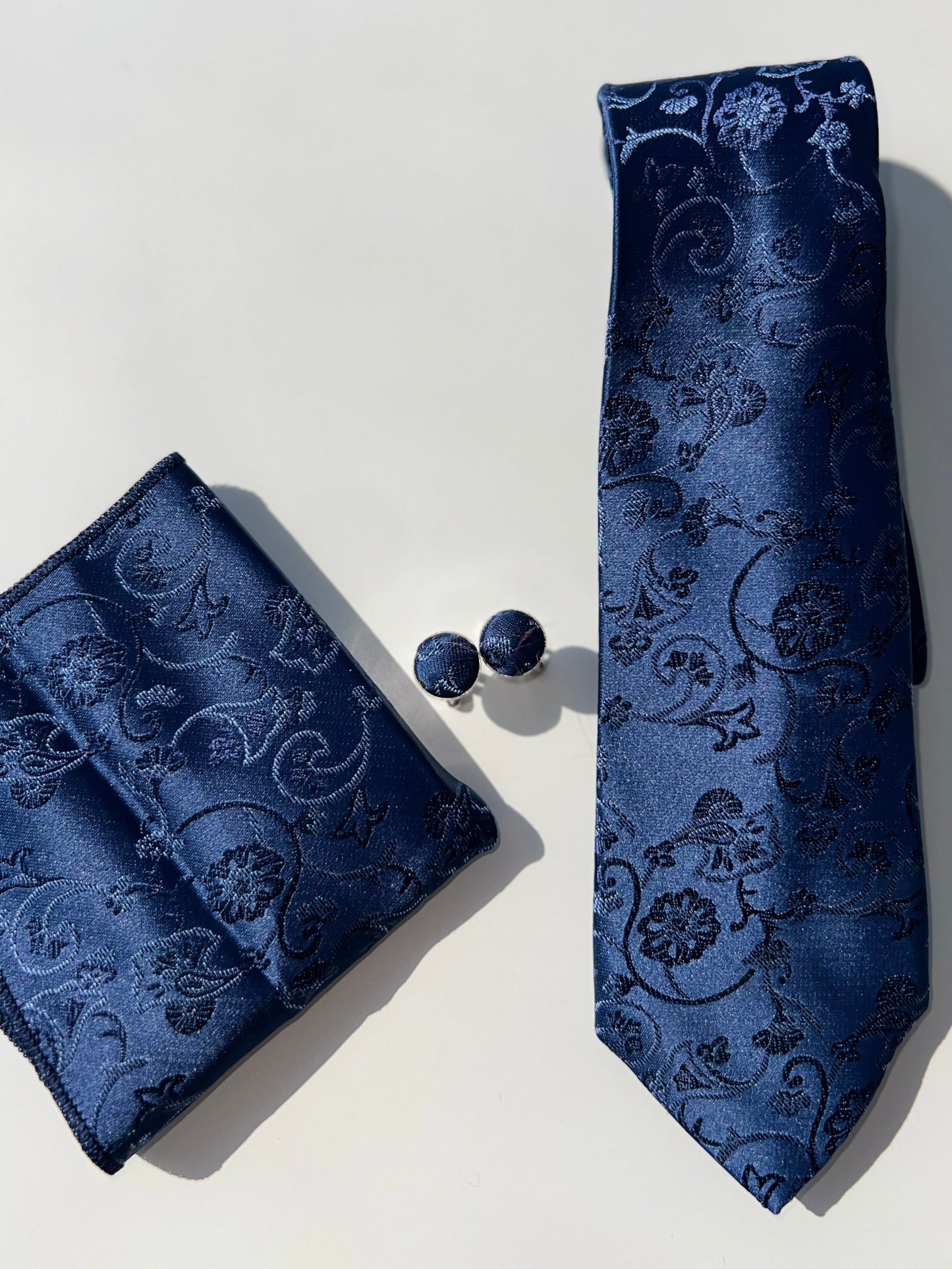 Navy blue paisley silk tie with matching pocket square and cufflinks set on a white background