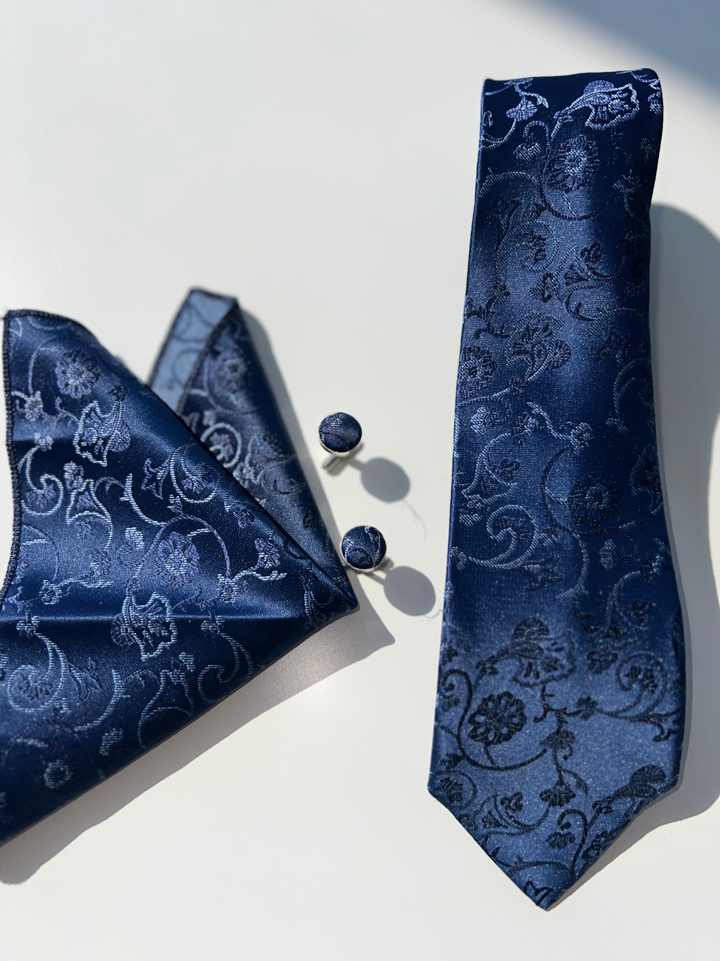 "Navy blue paisley tie draped next to pocket square and cufflinks, showcasing the cohesive design