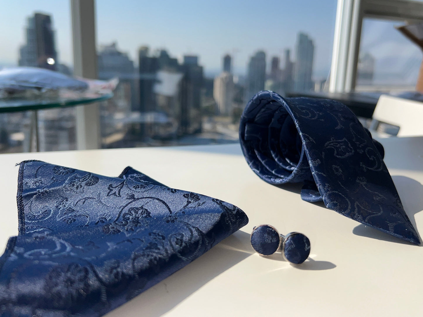 Full view of navy blue paisley tie set including tie, pocket square, and cufflinks on a reflective white table