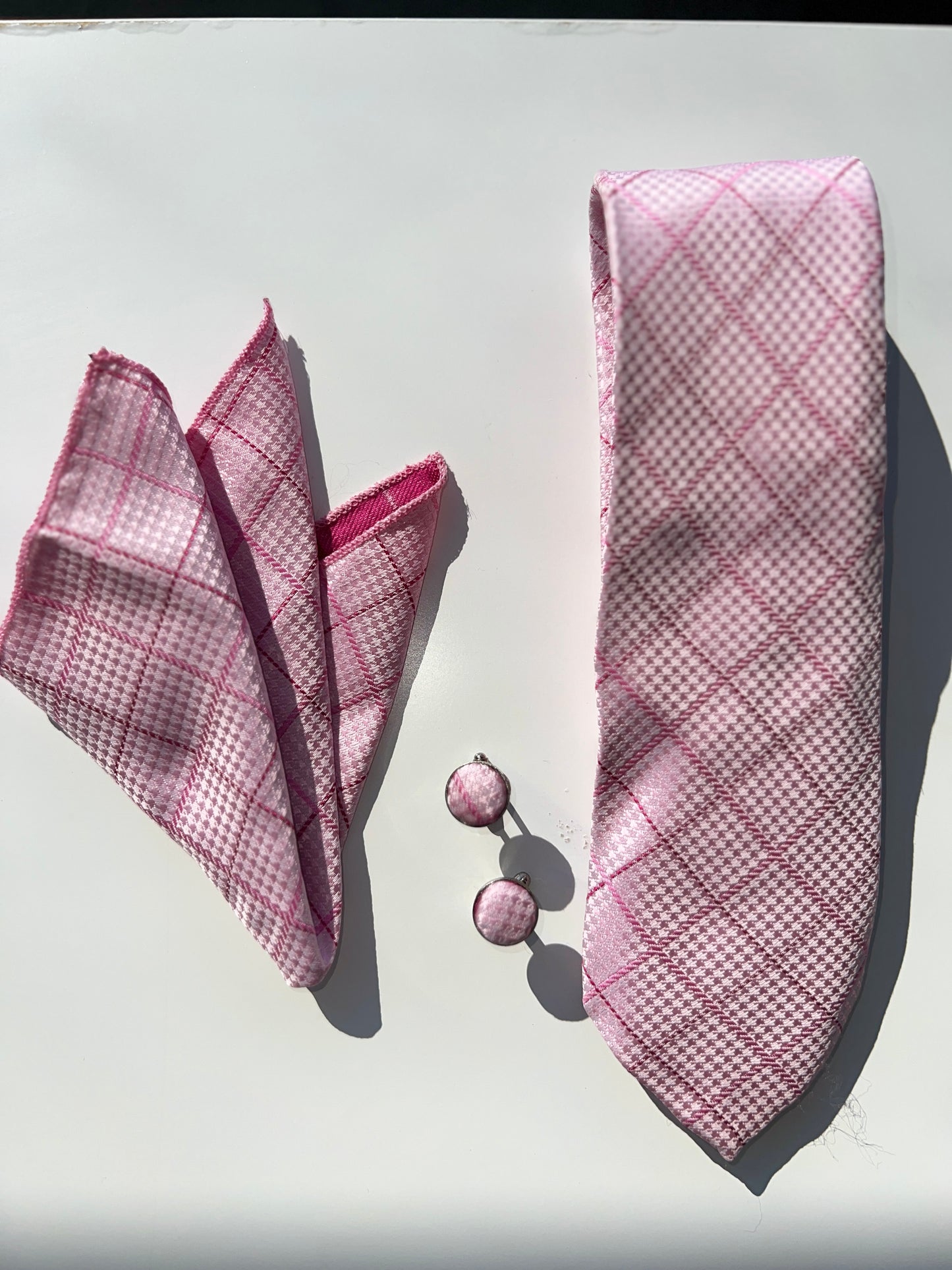 Full display of a pink tie set with a pocket square and cufflinks on a reflective surface, showcasing the intricate pattern and elegant design.