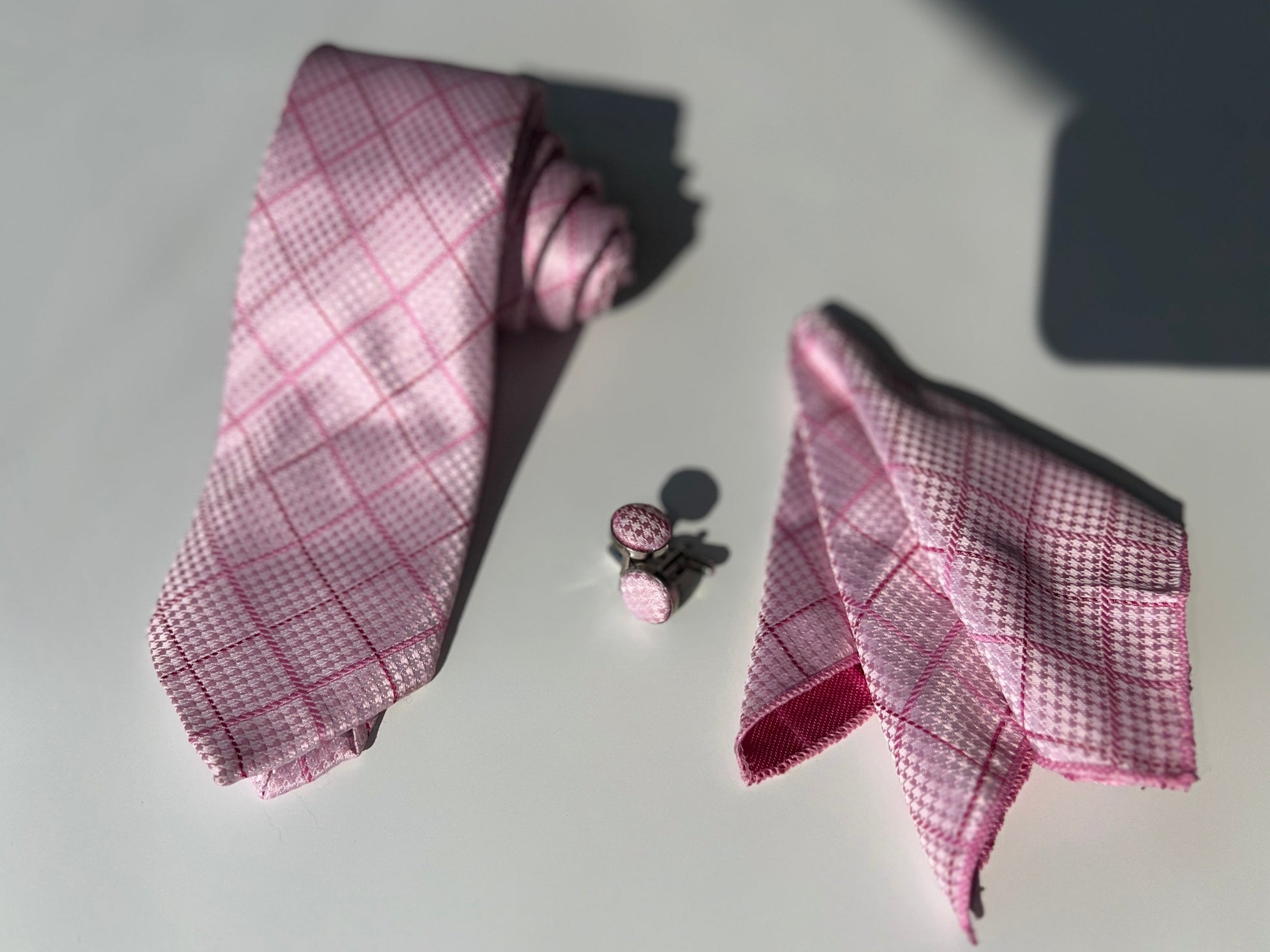 Full display of a pink tie set with a pocket square and cufflinks on a reflective surface, showcasing the intricate pattern and elegant design.