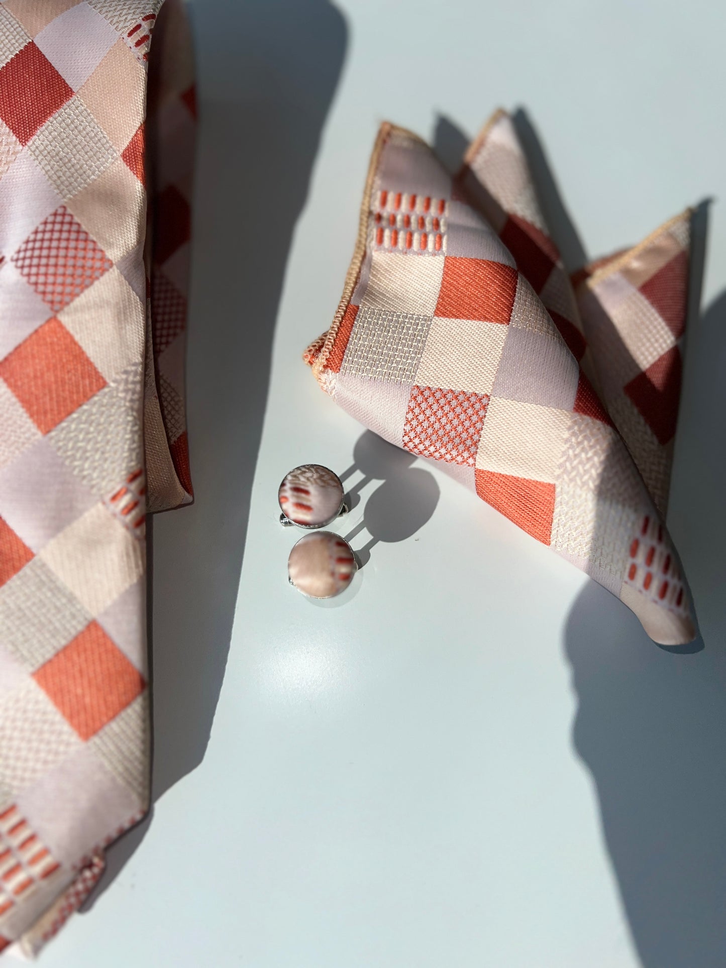 Orange and white geometric pattern silk tie with matching pocket square and cufflinks set on a clear background