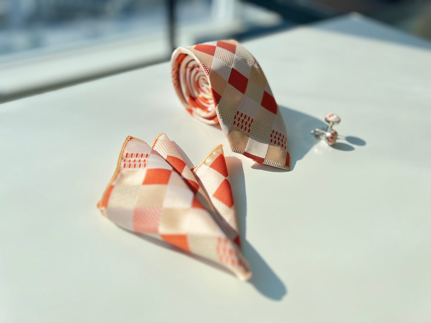 Orange and white geometric pattern silk tie with matching pocket square and cufflinks set on a clear background