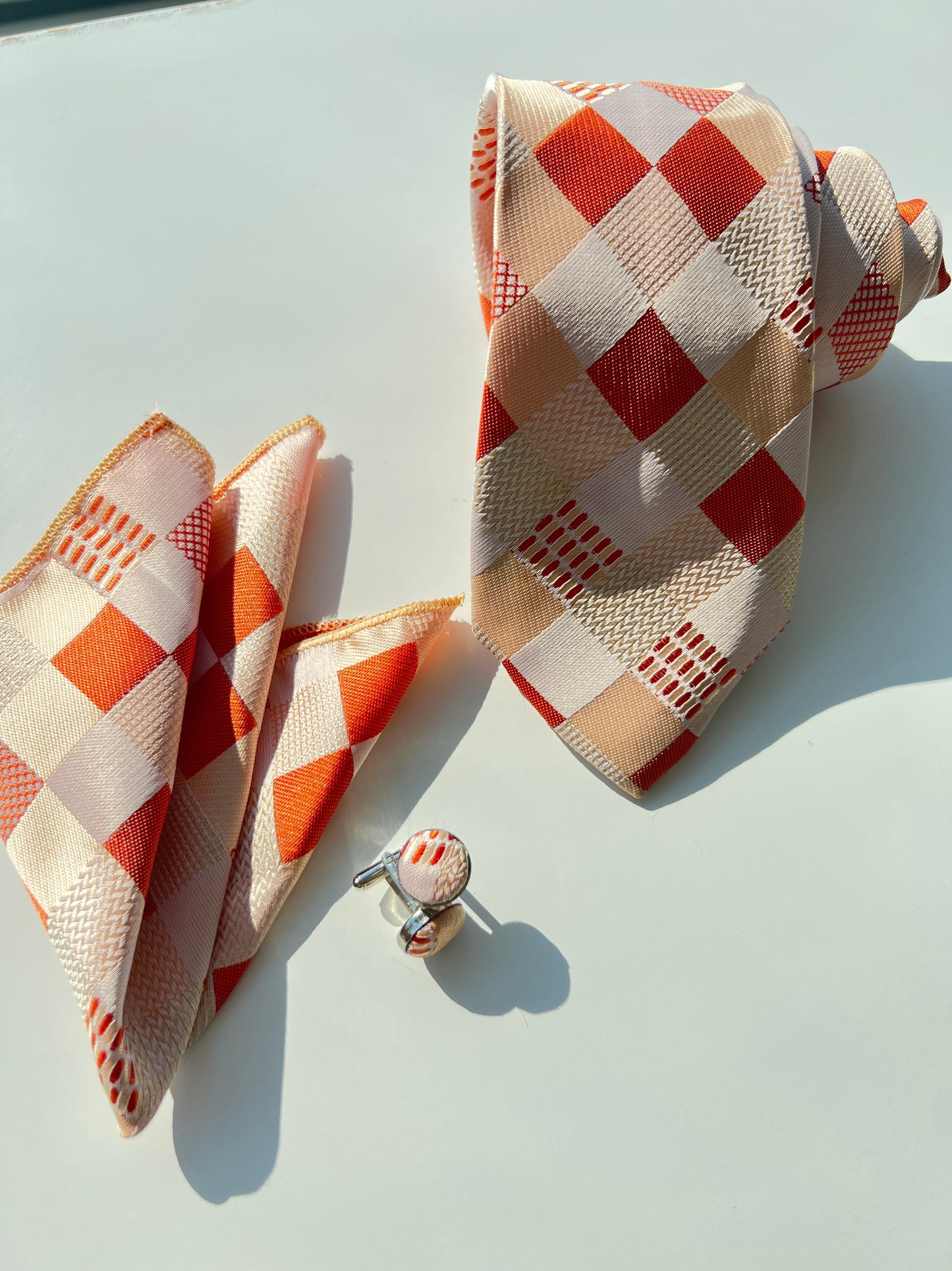 Orange and white geometric pattern silk tie with matching pocket square and cufflinks set on a clear background