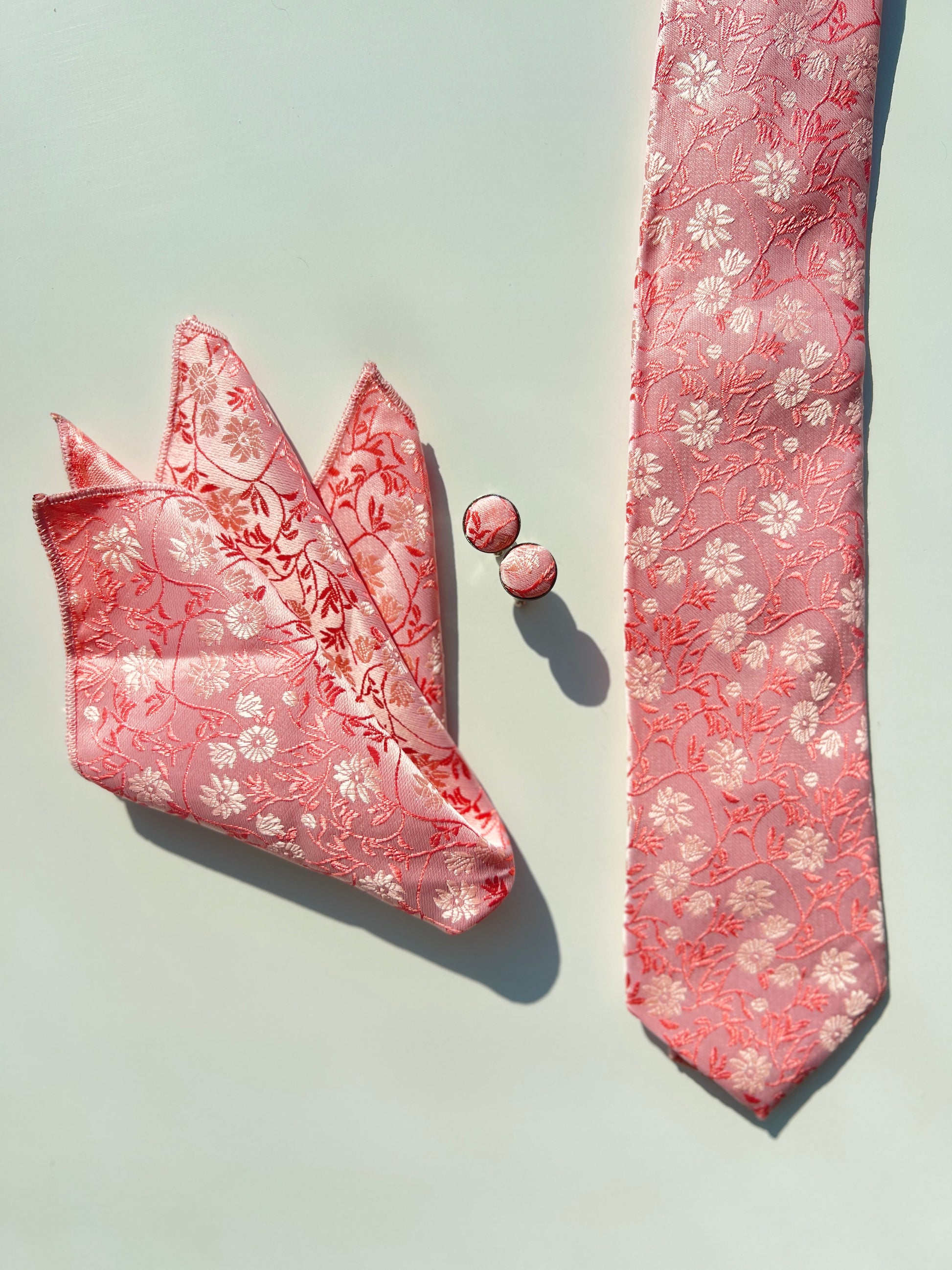 stylish floral pink tie set displayed on a sunny day, featuring a silk tie, a neatly folded pocket square, and a pair of cufflinks