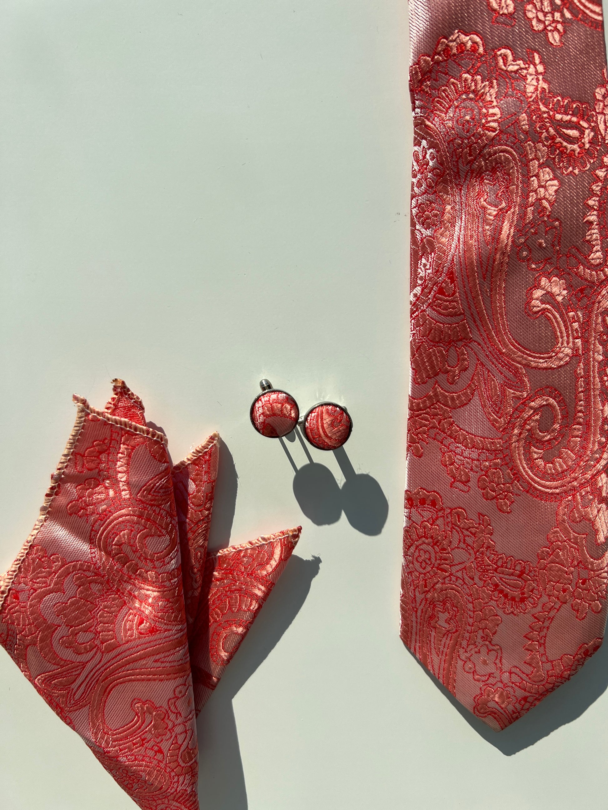 Regal red paisley silk tie with matching cufflinks and pocket square set on a clean background.